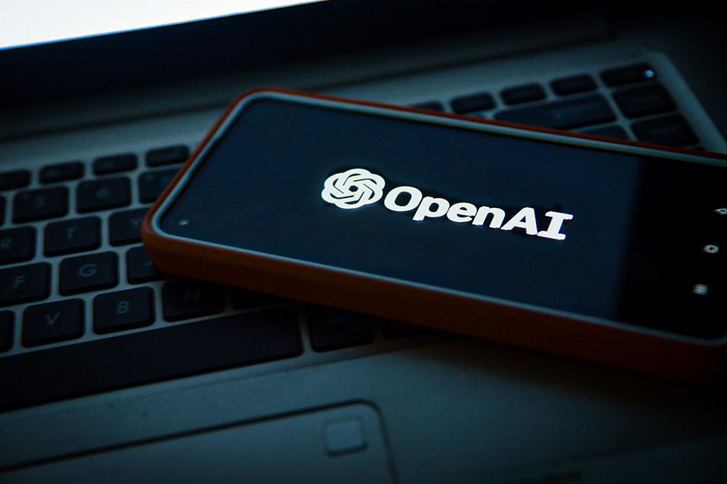 Um smartphone com capa laranja exibindo o logo e nome OpenAI em branco sobre tela preta, posicionado sobre um teclado de notebook cinza escuro